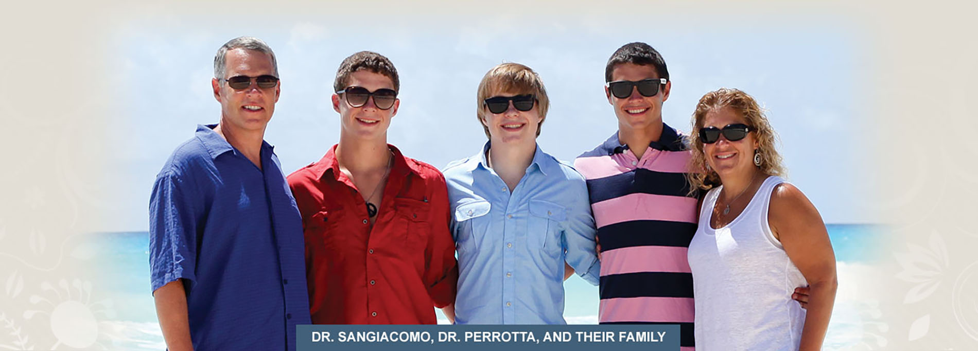 The image shows a group of five people posing together on a beach with clear skies, wearing colorful shirts and sunglasses, standing against a backdrop of the ocean.