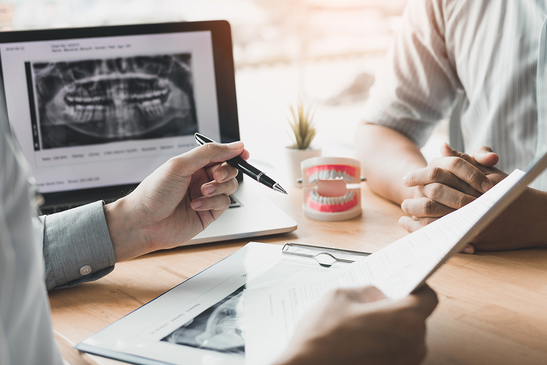 The image shows two individuals sitting at a table with a laptop displaying medical images, one person appears to be taking notes while the other seems to be reviewing the images.