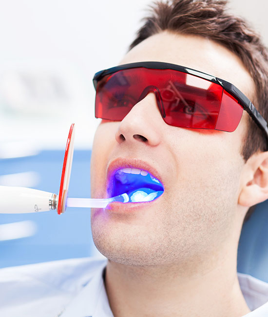 The image shows a person sitting in a dental chair with a bright blue light around their mouth, possibly indicating an ongoing dental procedure or treatment.